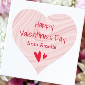 Heart shaped sticker with custom name and text "Happy Valentine's Day" on a blush pink satin swirls background