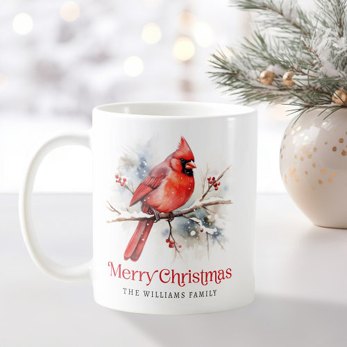 Personalized ceramic Christmas mug featuring a watercolor red cardinal perched on a snowy branch with red berries, festive Merry Christmas text, and customizable family name, perfect holiday gift idea.