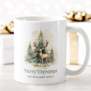 White ceramic Christmas mug featuring a watercolor deer standing among pine trees with snow, personalized with family name and “Merry Christmas” text. Rustic woodland holiday coffee cup.